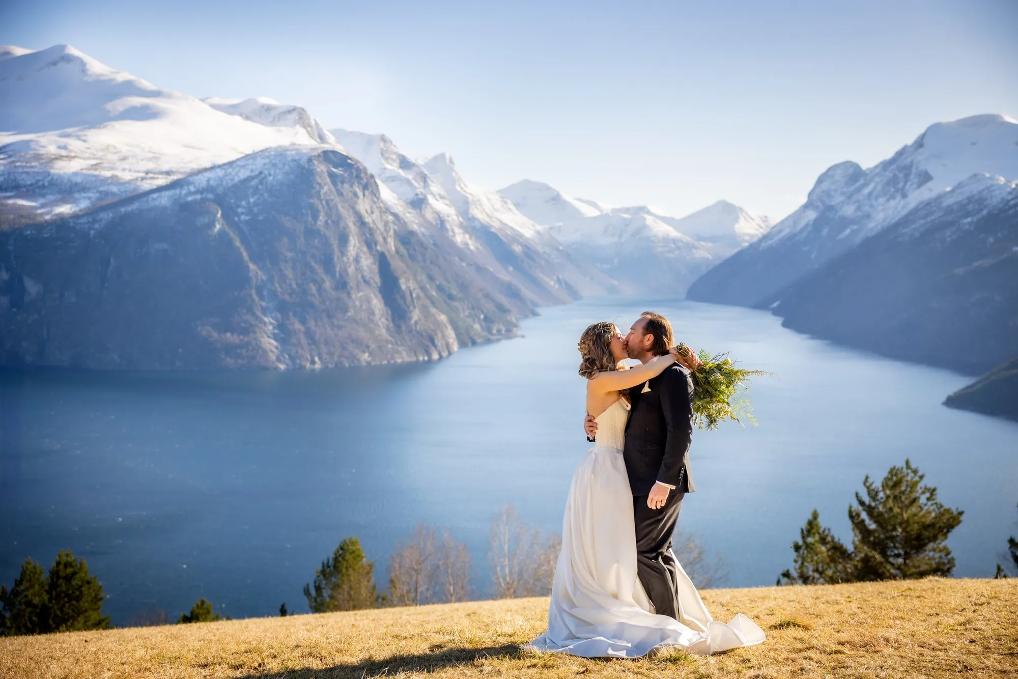 Brudepar kysser på et fjellplatå over en snøkledd fjord, fotografert av Marte Bjørgum