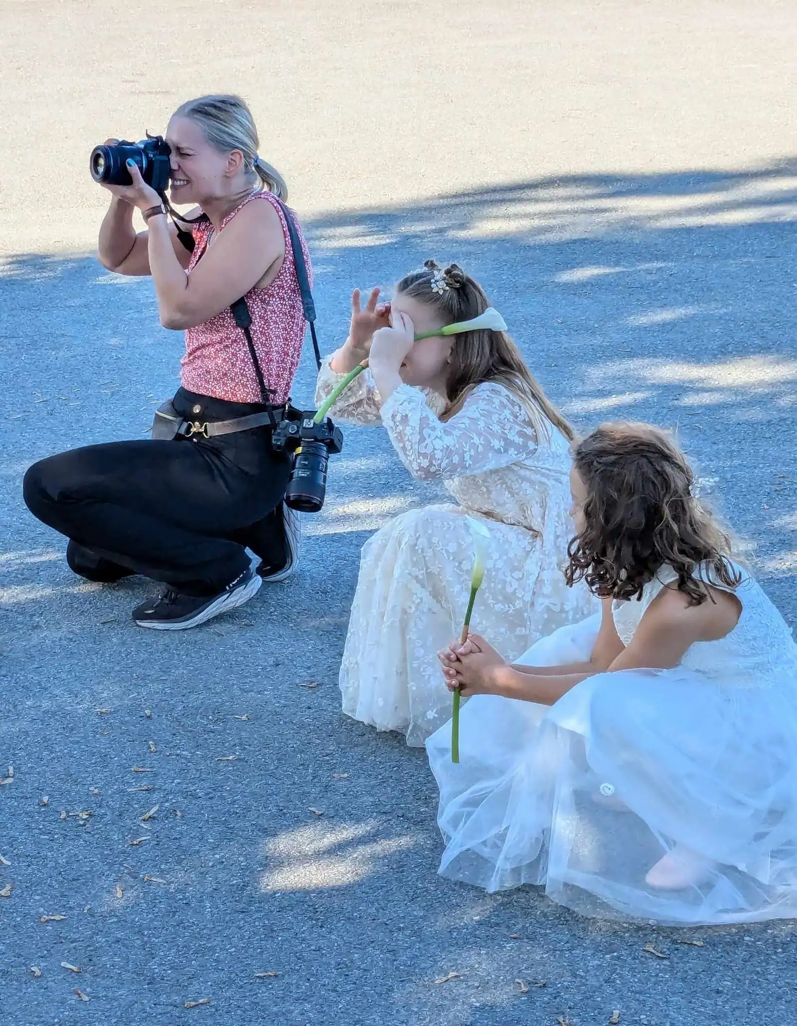 Marte Bjørgum på huk ute og fotograferer to brudepiker i hvite kjoler
