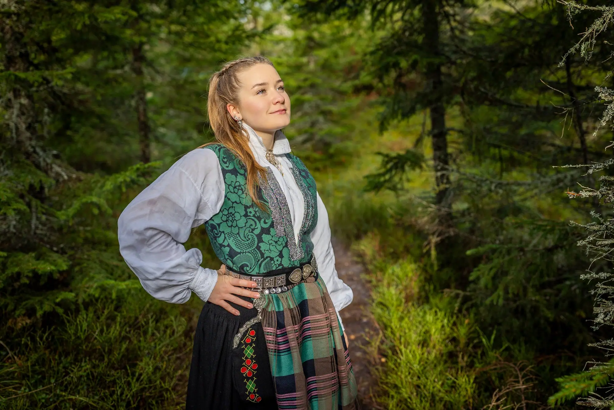 Konfirmant i bunad foran en foss, avslappet og naturlig